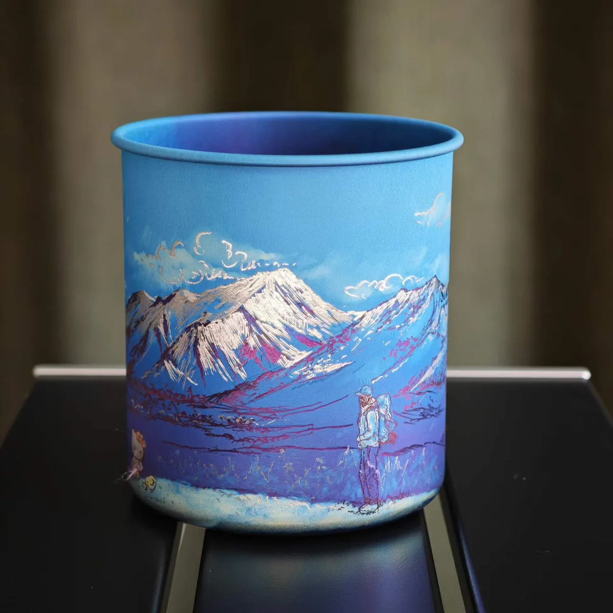 Camp mug painted with snowy mountains and a lone traveler