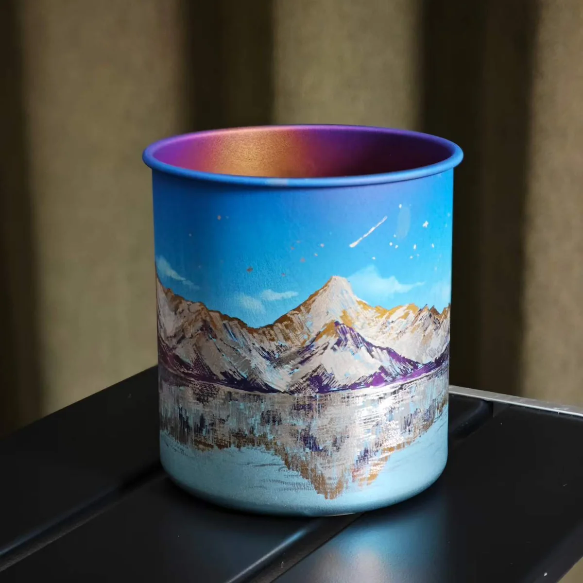 Camp mug painted with snowy peaks reflected in a lake