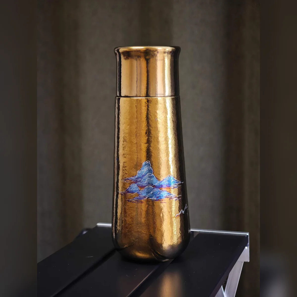 Gold hammered-texture bottle painted with small blue mountains
